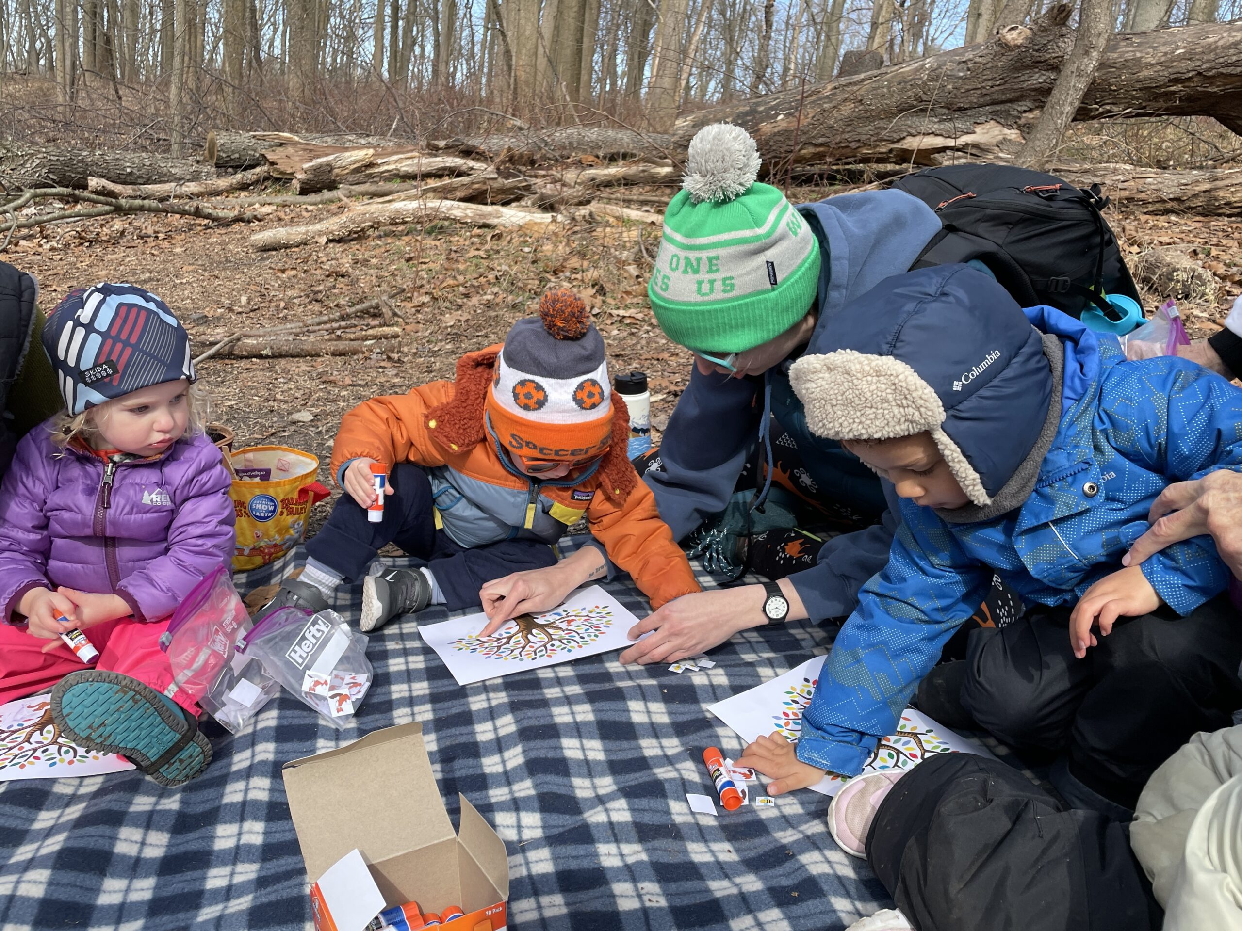 A group of children and one adult in winter clothes on a picnic basket in a winter forest.