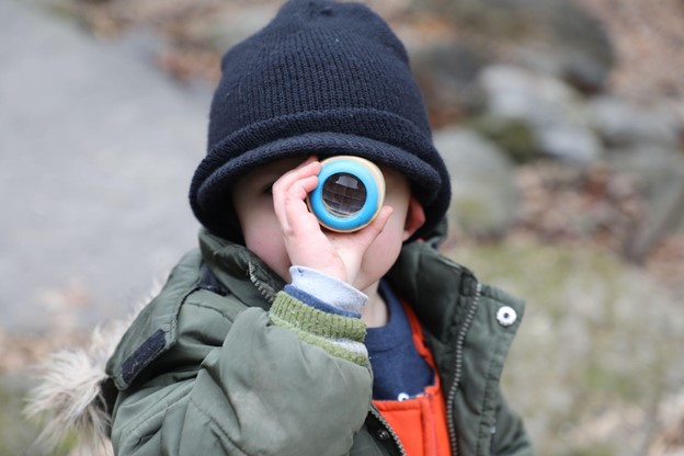 A child looks through a kaleidoscope wearing winter clothes outdoors.