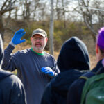 A man in blue gloves gives instructions to a group of volunteers.