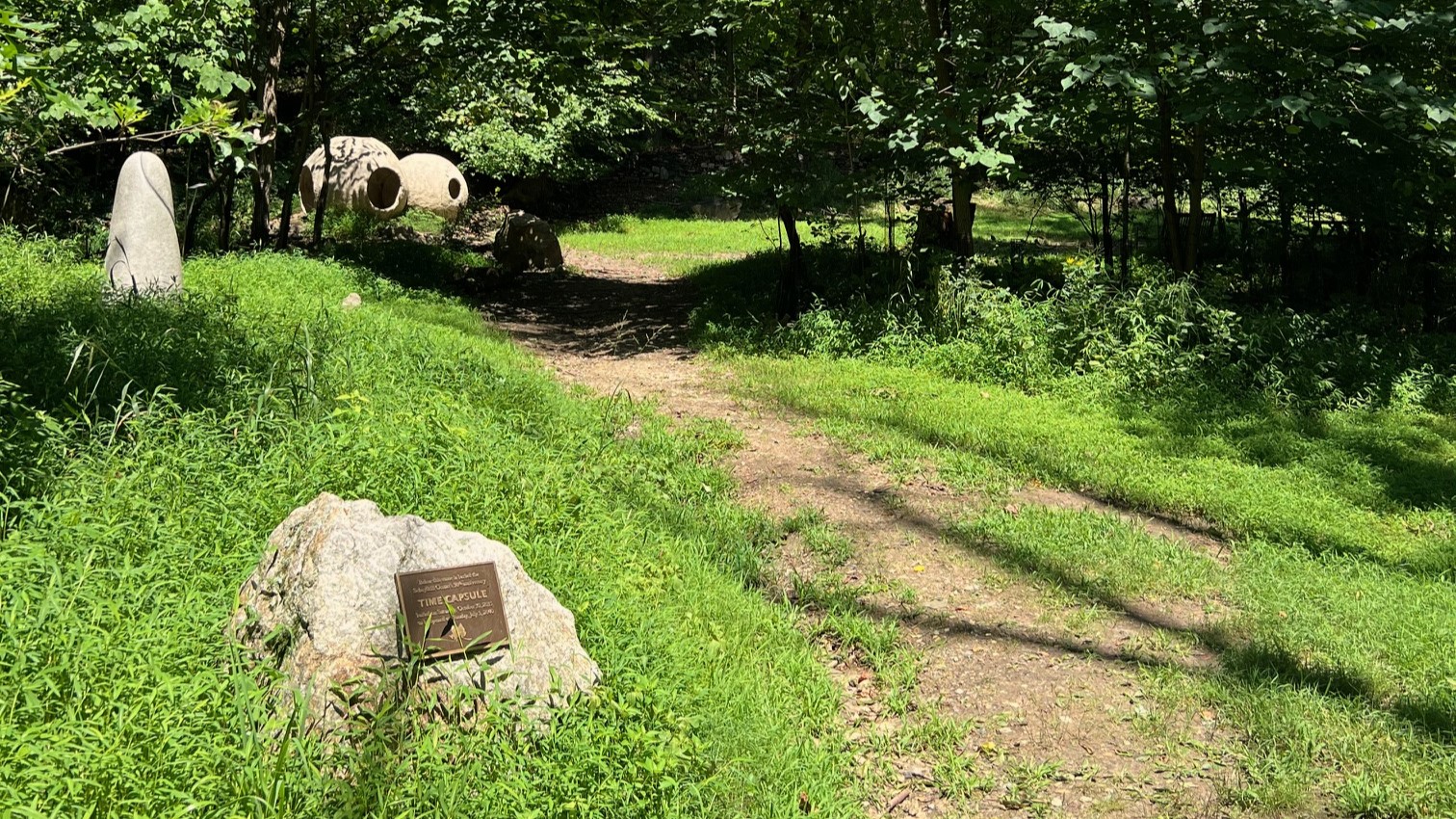 The trail to Jubilee Grove, a dirt trail next to a rock with a bronze sign.