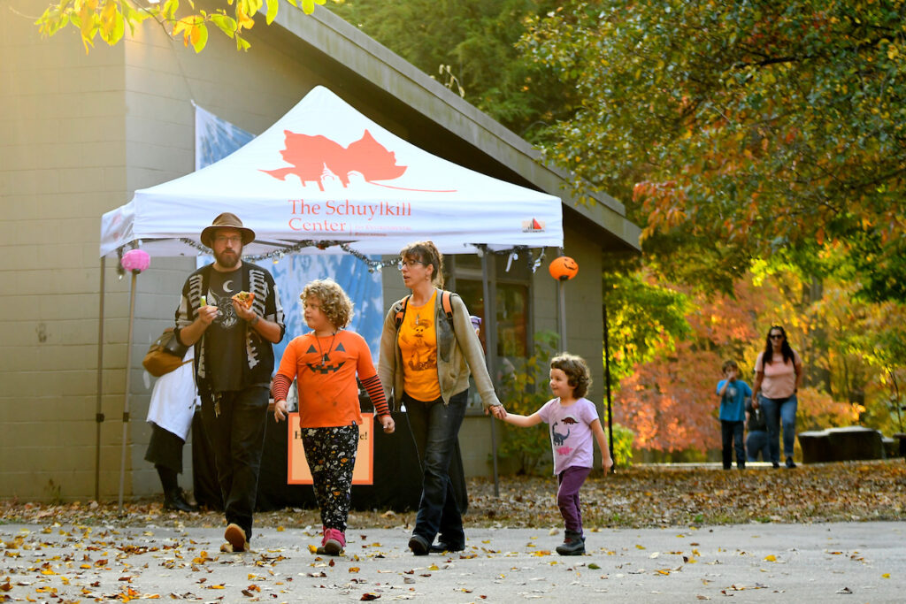 A family in Halloween t-shirts walks through the Schuylkill Center during their fall festival, Halloween Hikes and Hayrides.