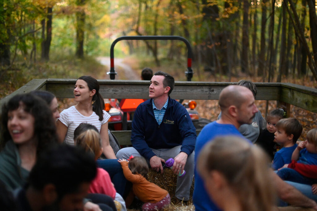 Families on a hayride through an autumn forest.