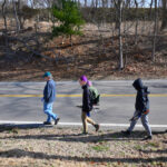 A group of people walking beside the road carrying hand tools in the winter.