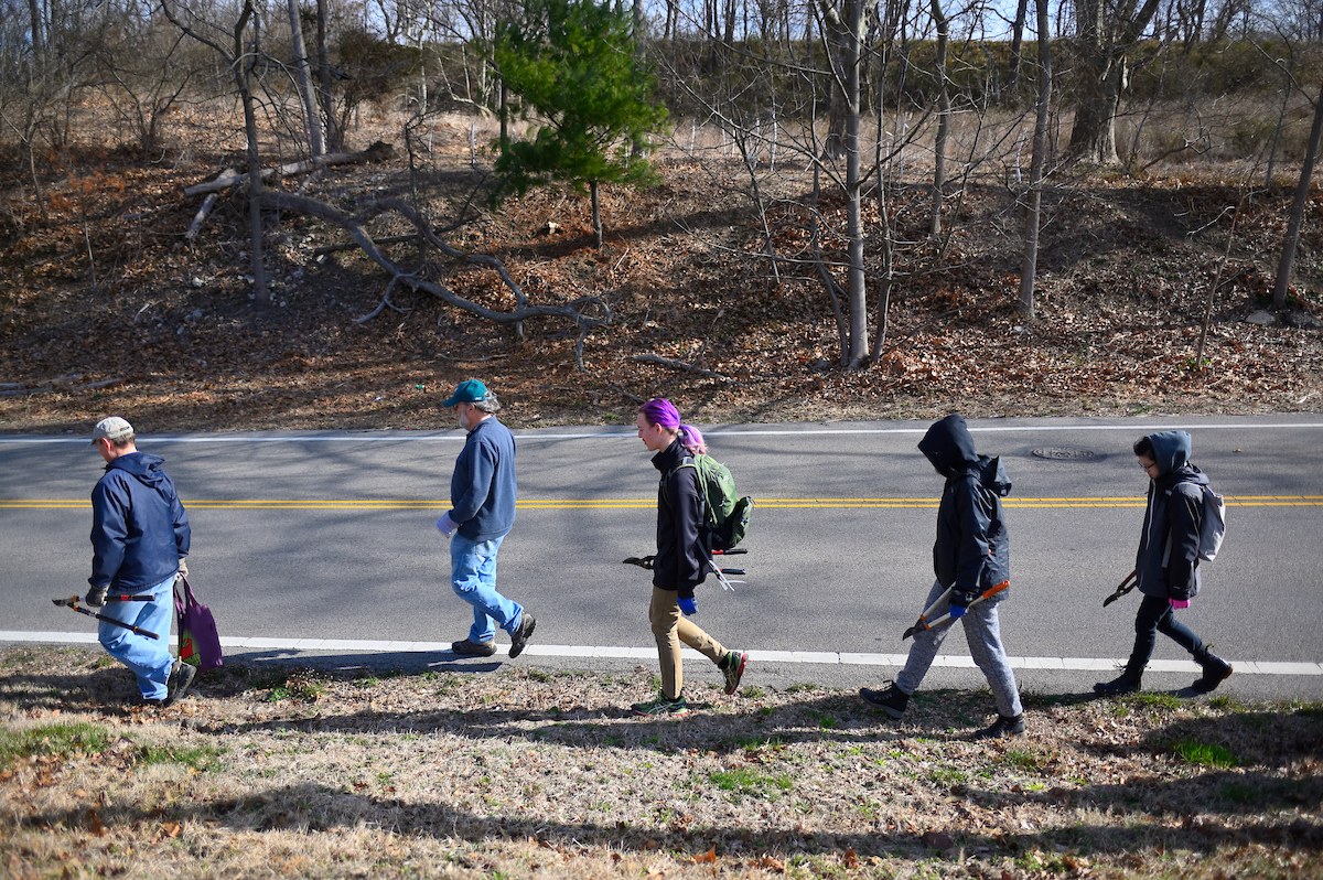 A group of people walking beside the road carrying hand tools in the winter.