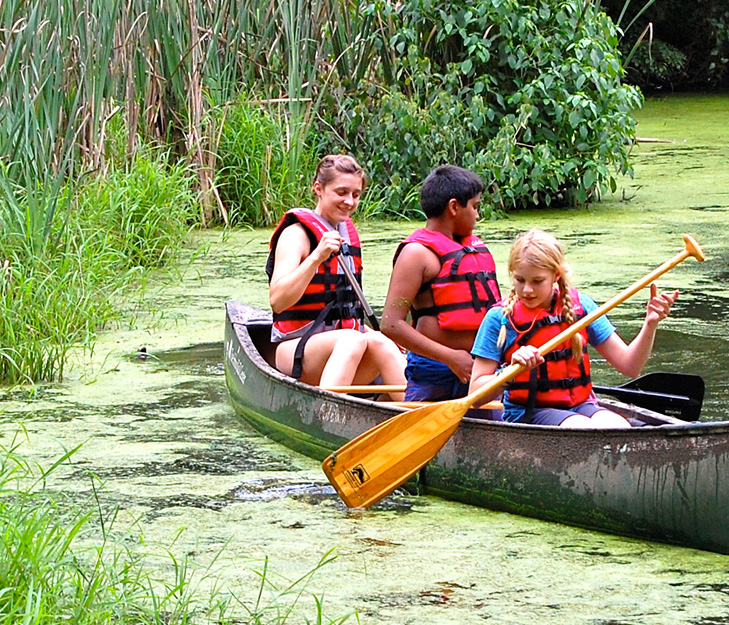 Three kids paddling in a canoe outdoors.