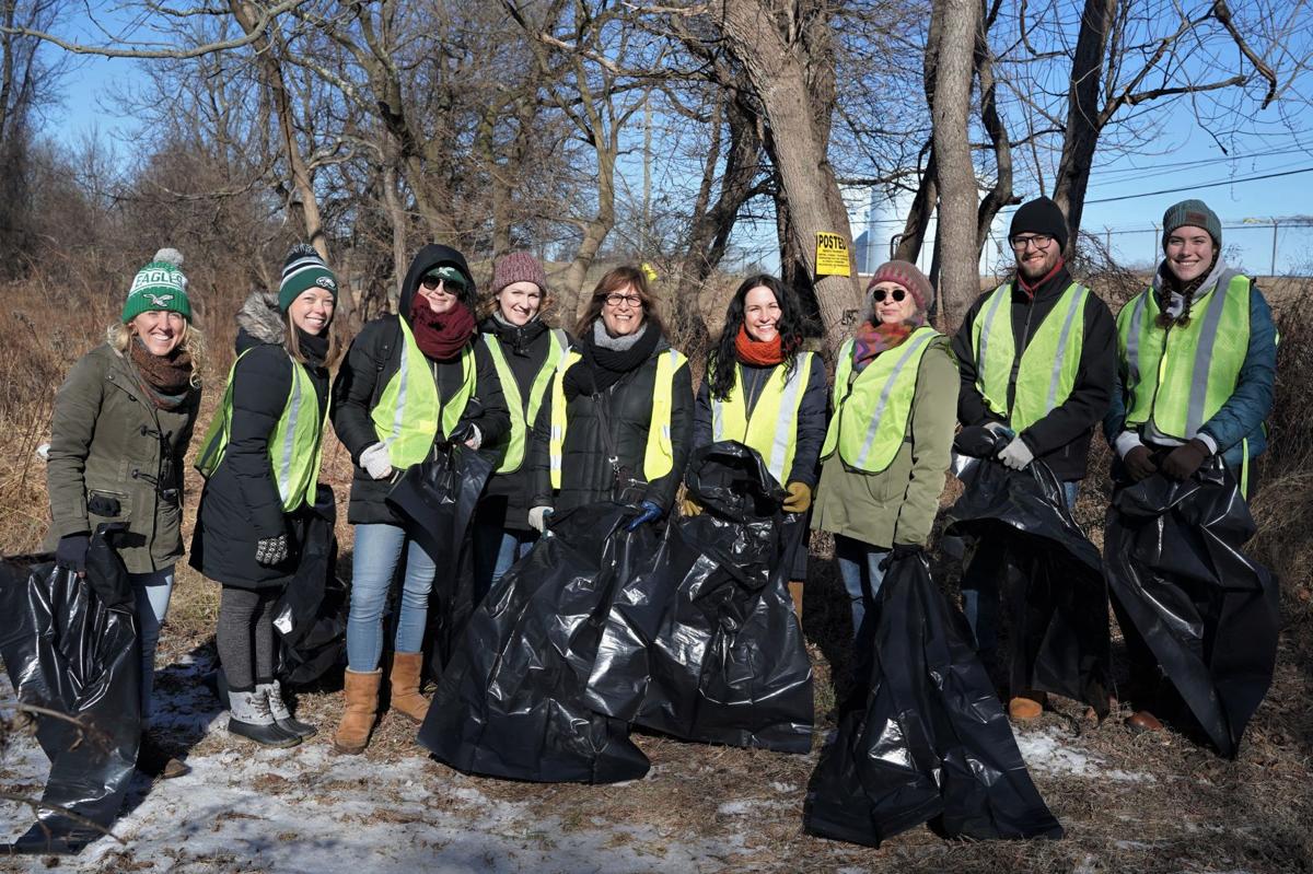 A group of volunteers wearing yellow vests hold trash bags and smile outdoors in the winter.