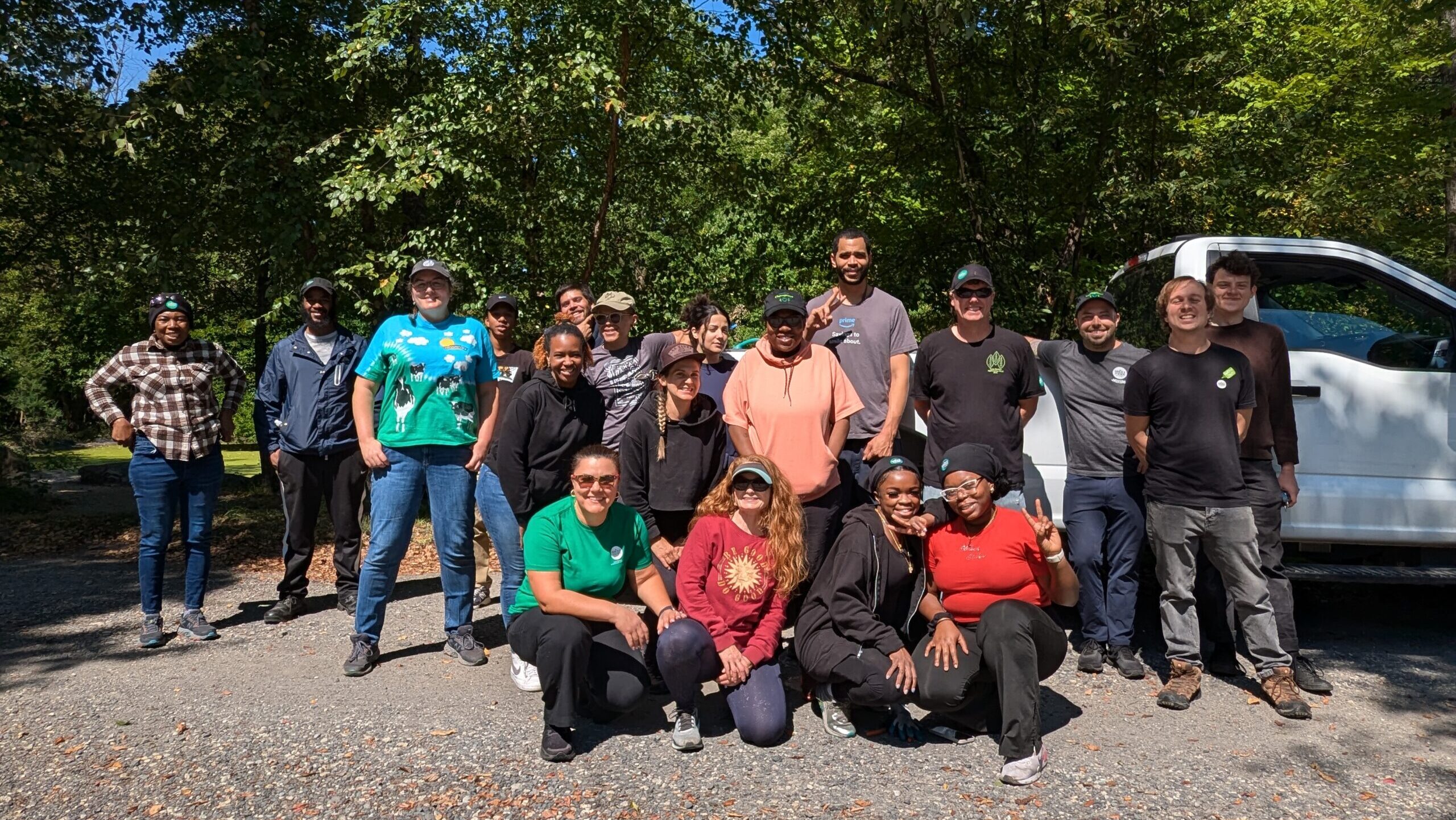 A group of volunteers stand and kneel outdoors next to tall trees.