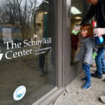 A child looks at the logo of the Schuylkill Center while an adult cleans glass on a door.