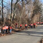 A group of volunteers wearing orange vests clean up trash along side of the road on a winter day.