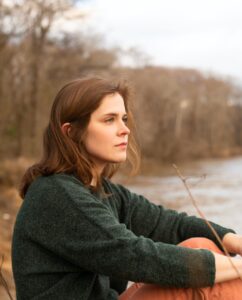 Portrait of artist Claire Downes Whitehurst sitting outdoors looking to the right.