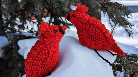 Two knitted cardinals on a snow covered branch.