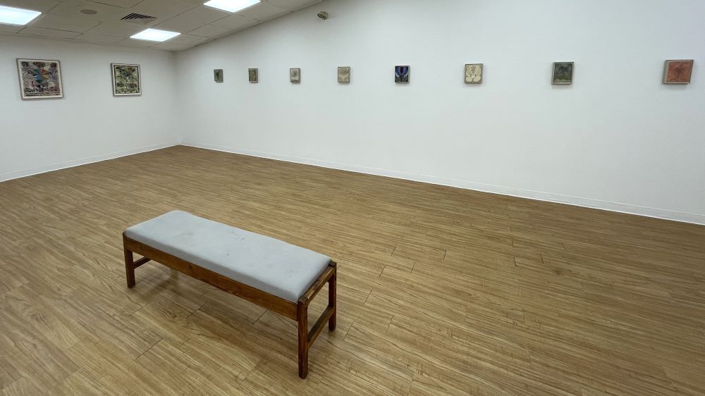 The gallery display for Winterbloom, a series of prints by artist Claire Downes Whitehurst in a white room with a wooden floor and a wooden bench in the center.